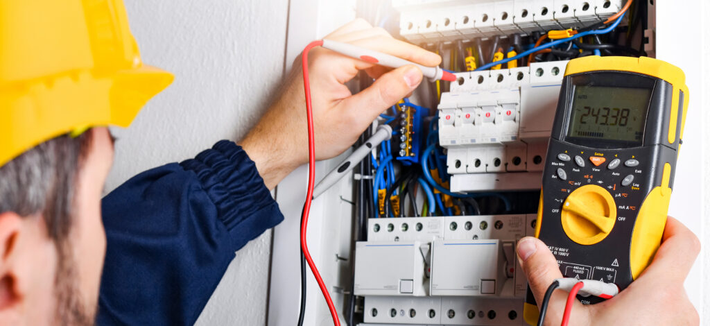 Electrician installing electric cable wires and fuse switch box. Multimeter in hands of electricians detail